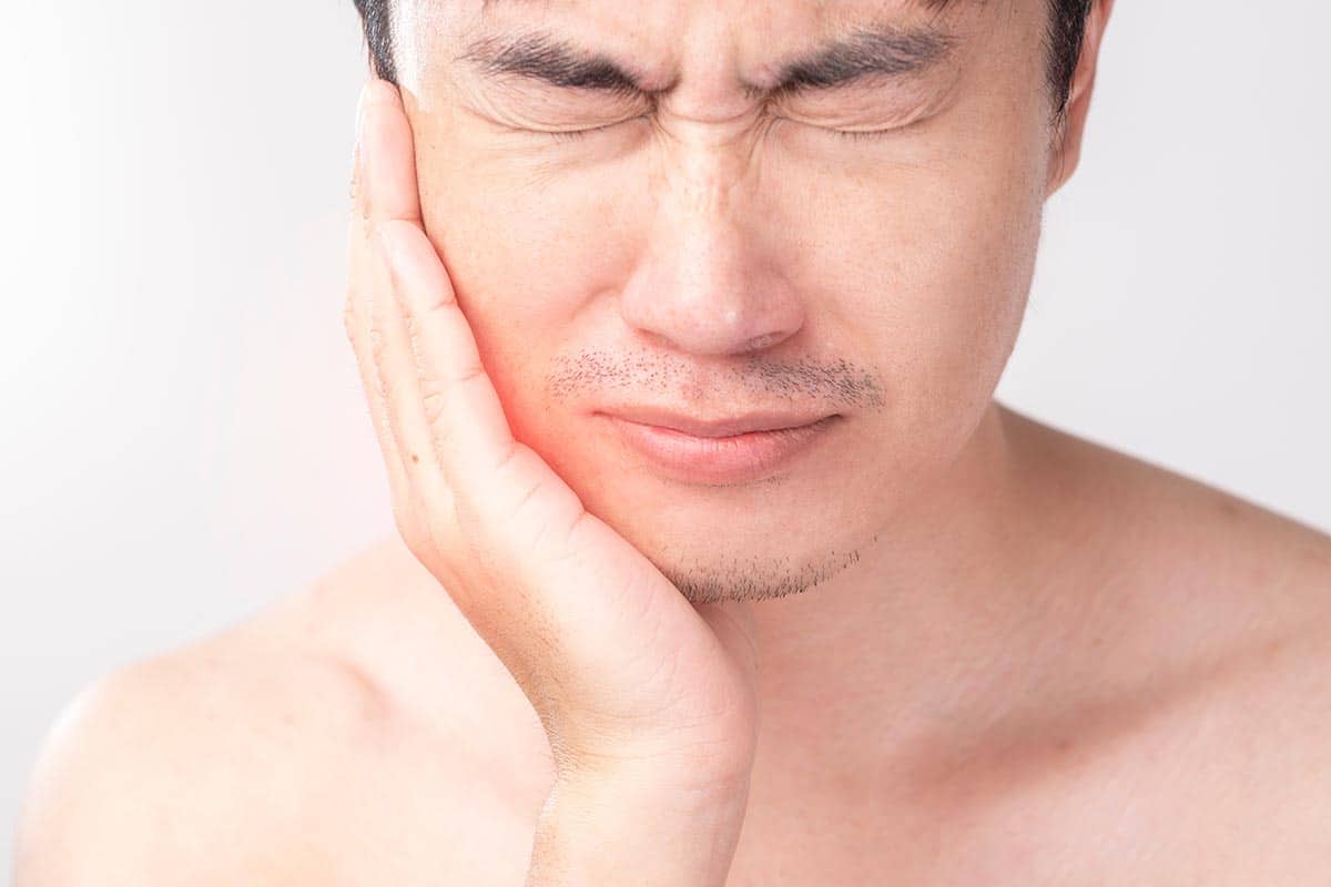 a man holding his cheek, experiencing wisdom tooth growing pains