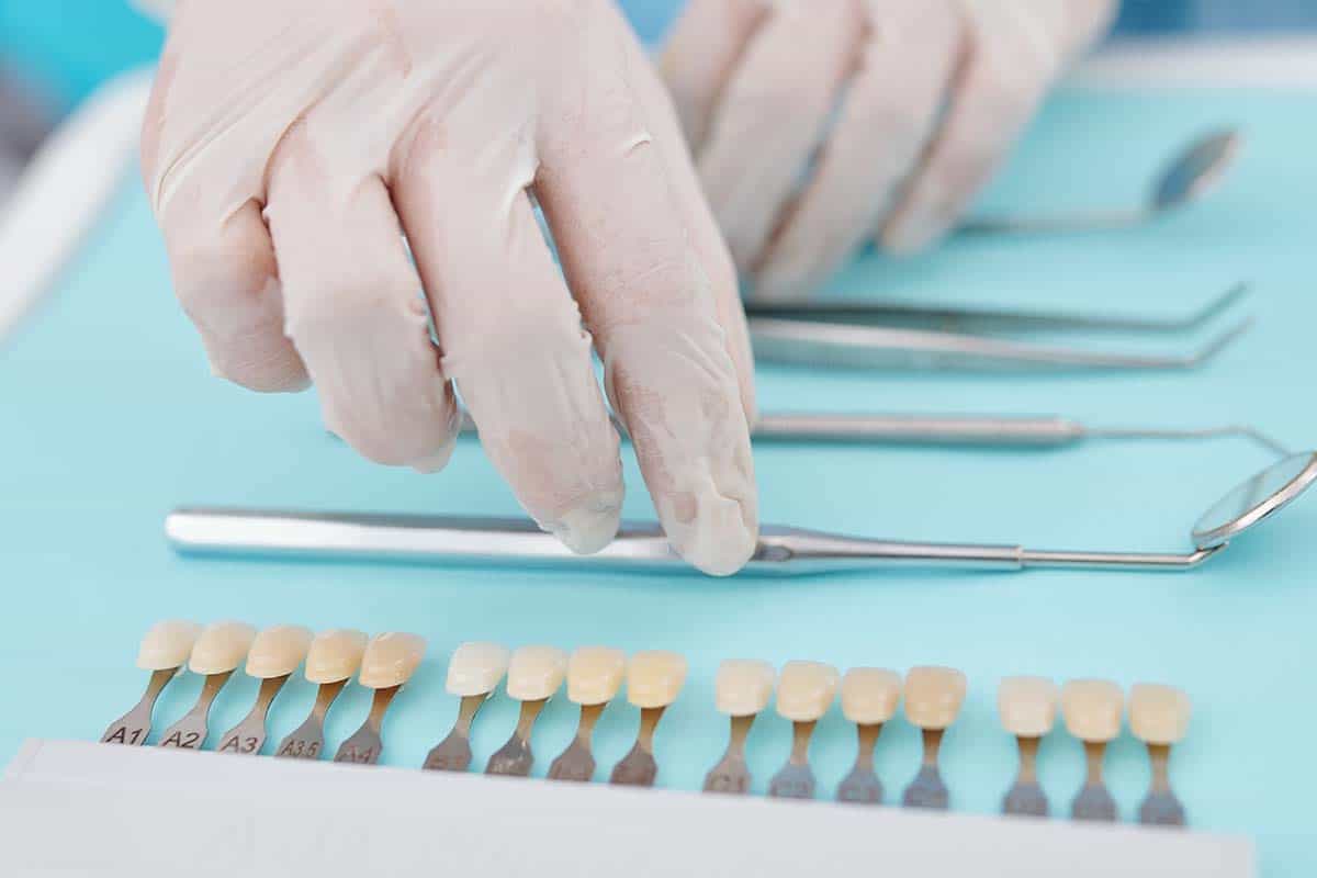 Hands of dentist in silicone gloves putting disinfected tools and veneers on the tray