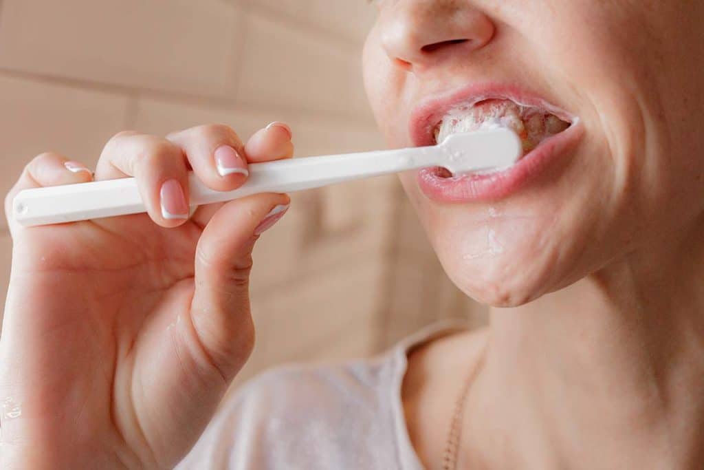 woman brushing her teeth to maintain results of teeth whitening treatment