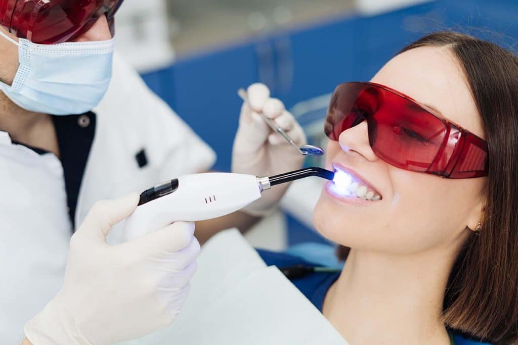 close up photo of a cosmetic dentist performing led teeth whitening on a young female patient